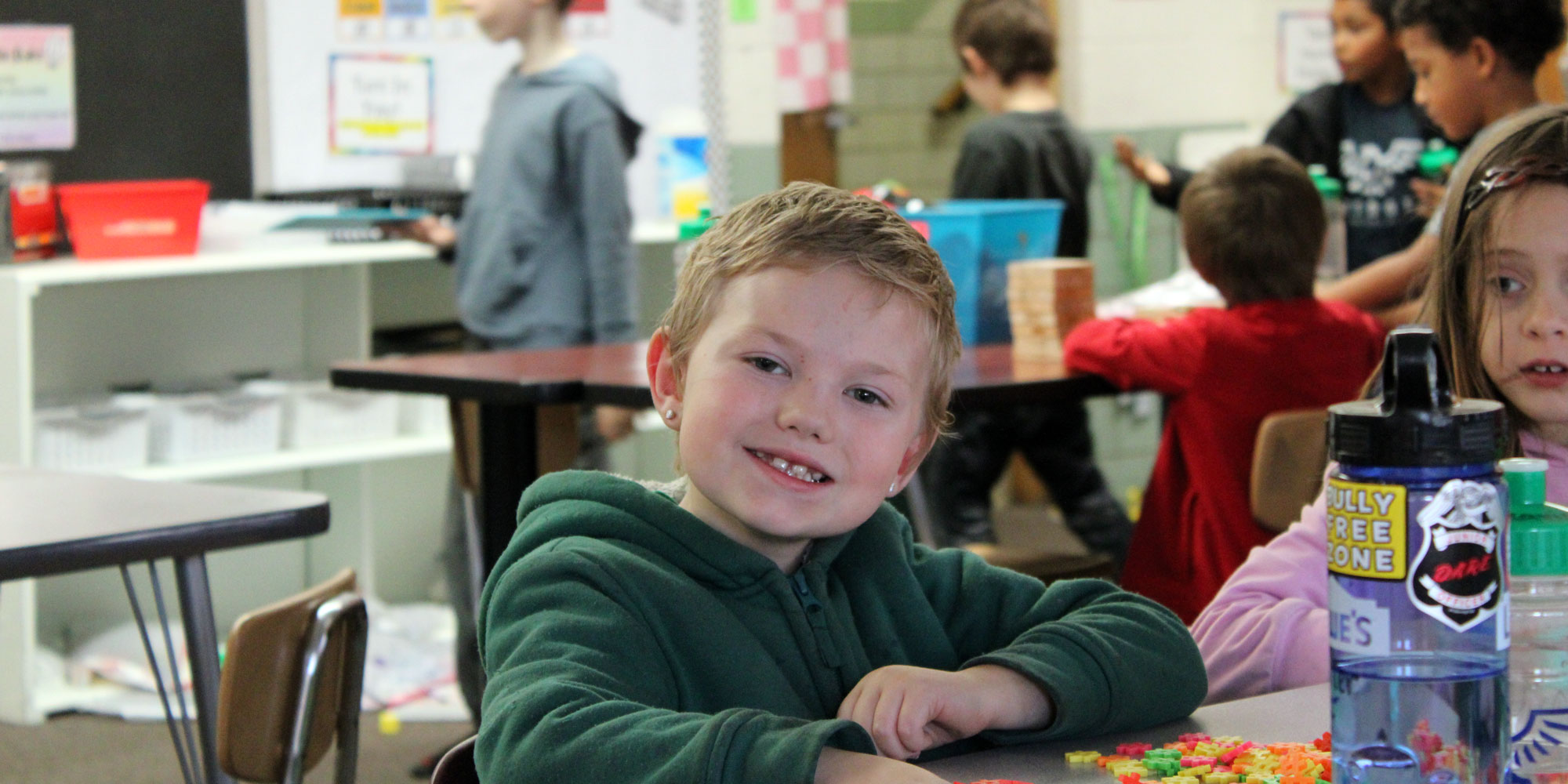 Smiling student in a green hoodie seated at a classroom table.